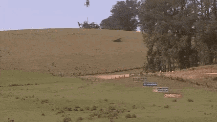 a helicopter is flying over a dirt road while a race car is driving down it .