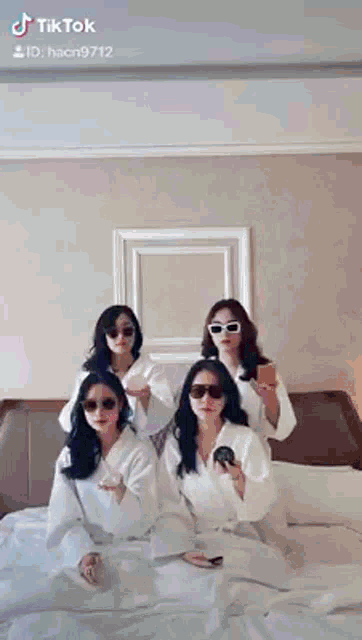 a group of women wearing bathrobes and sunglasses are sitting on a bed .