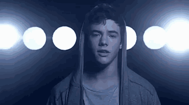 a young man wearing a hoodie is standing in front of a row of lights in a dark room .