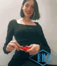 a woman in a black top is smiling and holding a red object in her hands