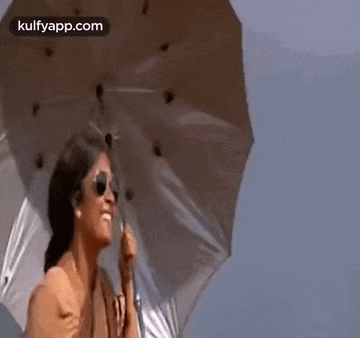 a woman in sunglasses is holding an umbrella in the wind .