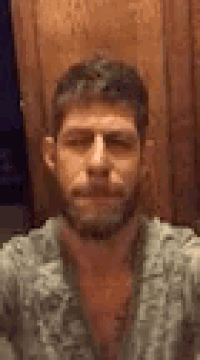 a man with a beard is taking a selfie with his eyes closed and a wooden wall in the background .