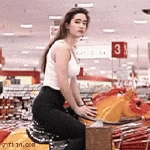 a woman in a white tank top is riding a carousel horse in a store ..