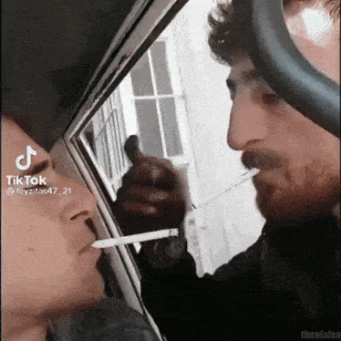 a man is smoking a cigarette next to another man in a car .