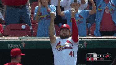 a man in a cardinals jersey stands in front of a mercy sign
