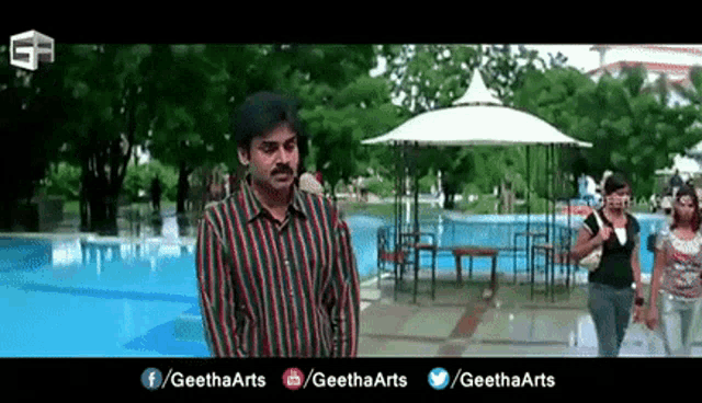 a man in a striped shirt is standing next to a swimming pool .