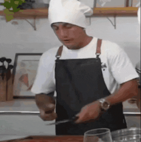 a man wearing an apron and a chef 's hat is cutting something with a knife
