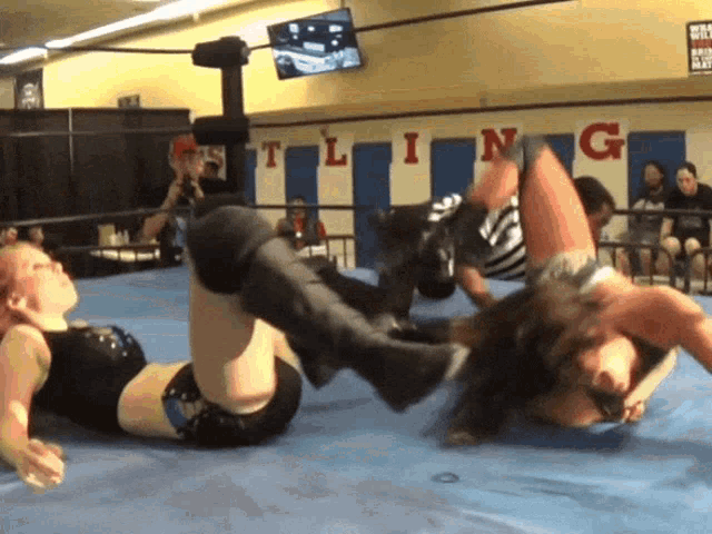 two women are wrestling in a ring with the word tling on the wall behind them