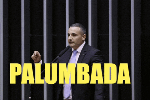 a man in a suit and tie stands in front of a microphone with the words palumbada written in yellow