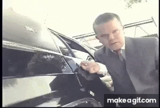 a man in a suit and tie is standing next to a black car holding a gun .