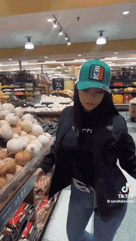 a woman is standing in a grocery store looking at coconuts .