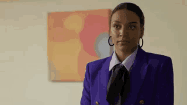 a woman in a purple suit and tie is standing in front of a painting on the wall .