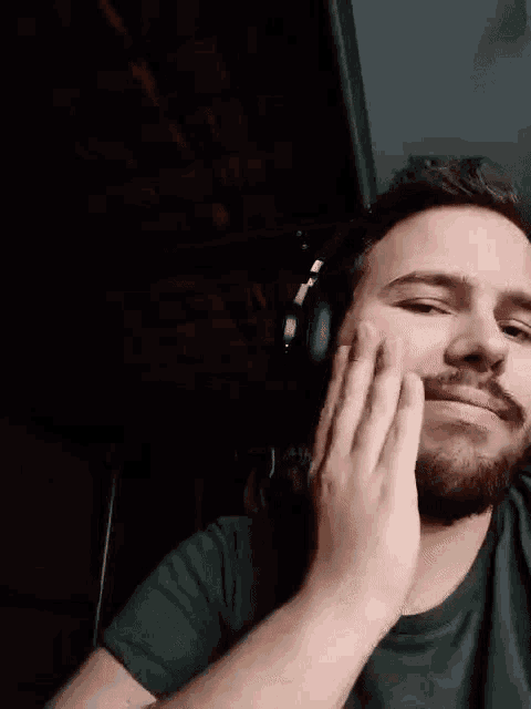 a man with a beard is wearing headphones and touching his face with his hands .