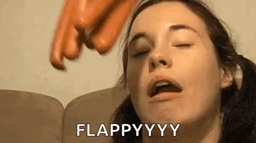 a woman is sitting on a couch with her eyes closed and a hot dog being thrown at her face .