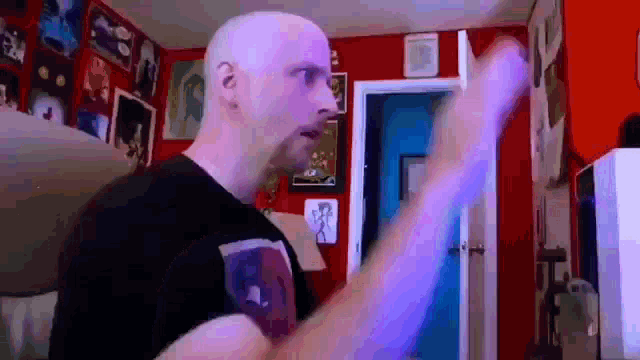 a bald man in a black shirt is standing in a room with a red wall and a door .