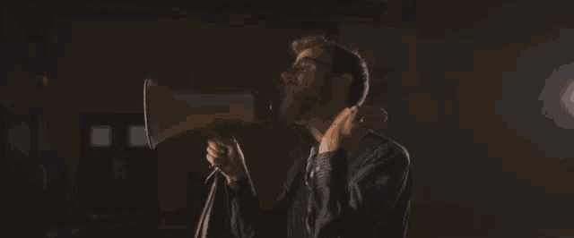 a man is holding a megaphone in his hand and shouting into it in a dark room .