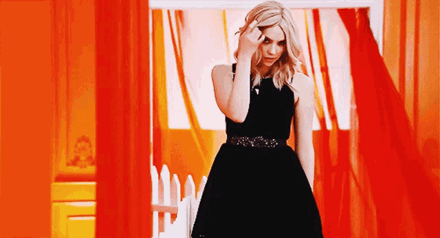 a woman in a black dress stands in front of an orange curtain