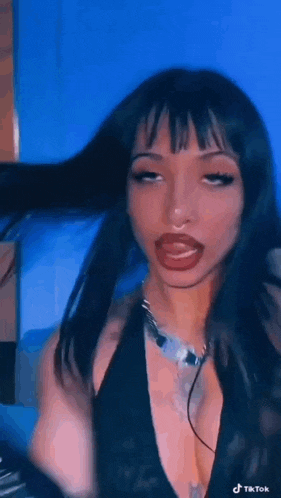 a woman with long black hair and red lips is making a funny face while wearing a black top and a necklace .