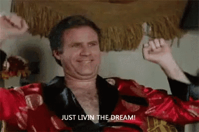 a man in a red robe is sitting in a chair with his arms in the air and saying `` just livin the dream '' .