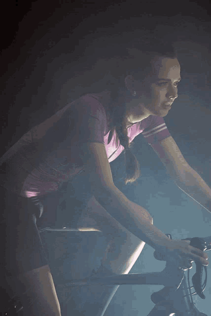 a woman in a pink shirt is riding a bike
