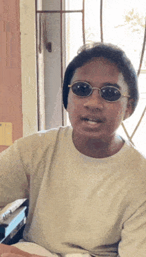 a man wearing sunglasses and a white shirt is sitting in front of a window .