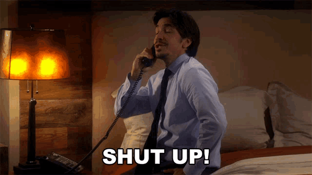 a man talking on a telephone with the word shut up written below him