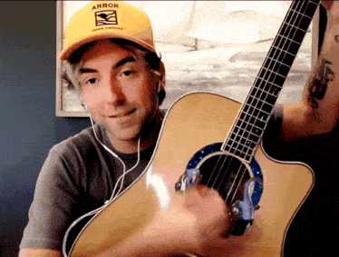 a man wearing a yellow hat that says arbor holds a guitar