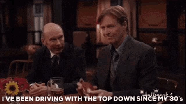 three men are sitting at a table drinking beer and one of them is saying i 've been driving with the top down since my 30