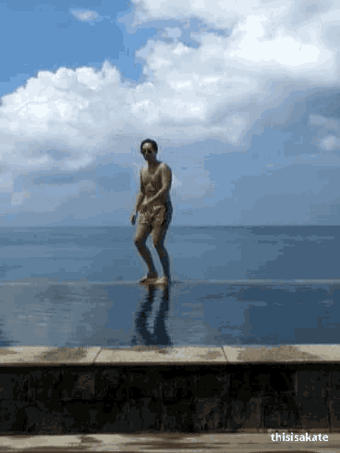 a man is standing on the edge of an infinity pool with the ocean in the background