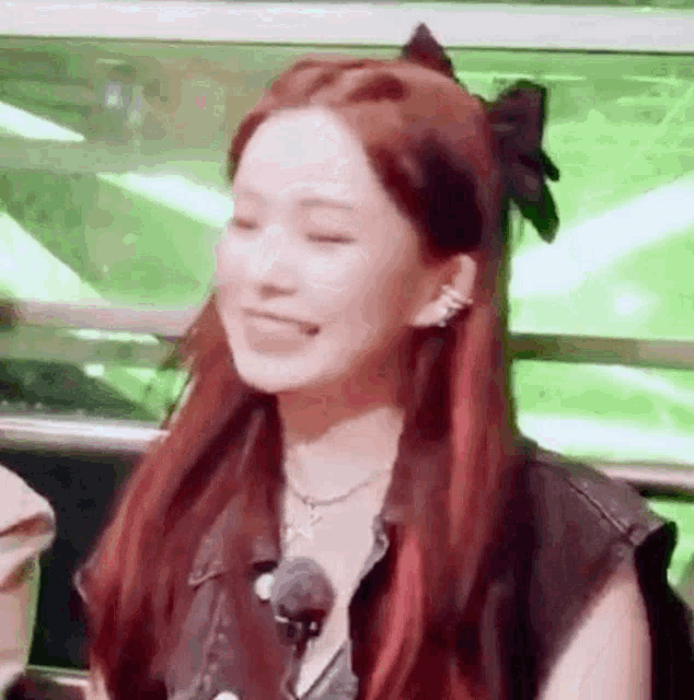 a woman with red hair and a bow in her hair is smiling and looking at the camera .