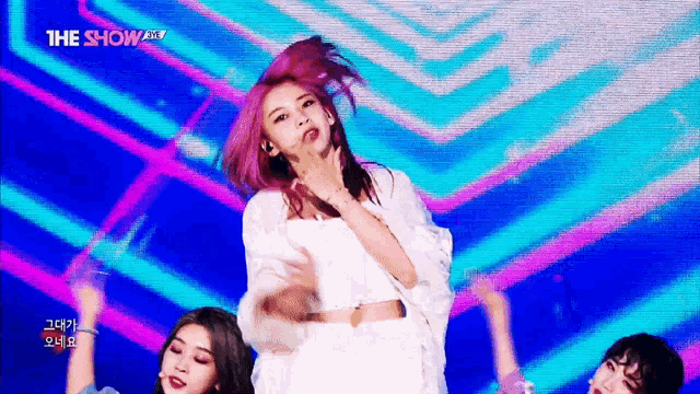 a woman with pink hair is dancing on a stage in front of a screen that says the show