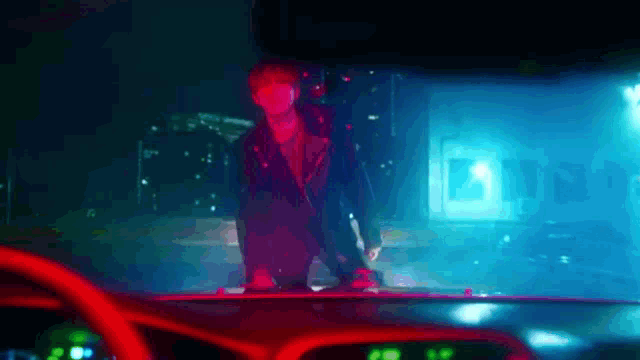 a man in a red jacket is standing on the roof of a car .