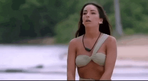 a woman in a bikini is standing on a beach with her eyes closed .