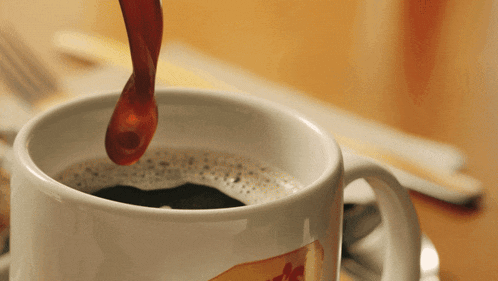a close up of a cup of coffee with syrup being poured from a spoon