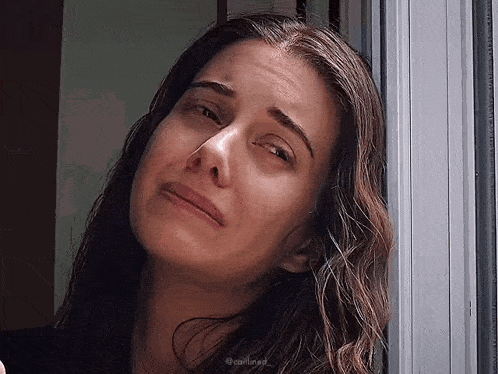 a woman is crying while looking out of a window and making a funny face .