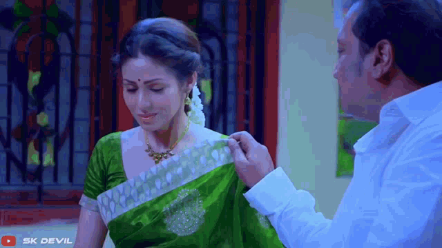 a woman in a green saree is sitting next to a man in a white shirt with sk devil written on the bottom