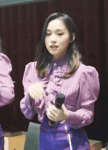 a woman in a purple ruffled shirt holds a microphone