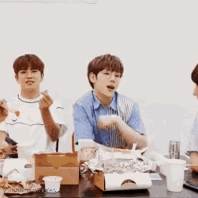 a group of young men are sitting at a table eating food and drinking .
