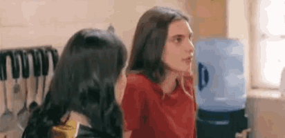 two women are sitting next to each other in a kitchen and talking to each other .