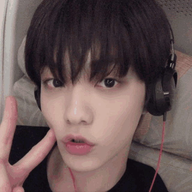 a close up of a person wearing headphones giving a peace sign