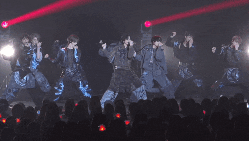 a group of people are dancing on a stage in front of a crowd with a red light behind them