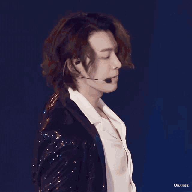 a man with long hair is wearing a microphone and looking up at the sky