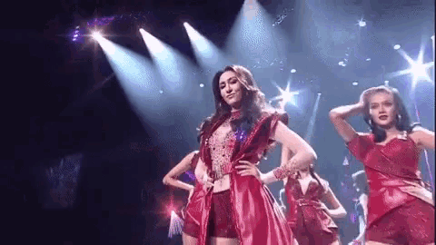 a woman in a red dress is dancing on a stage with other dancers .