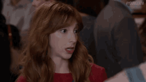 a woman with red hair is making a funny face while sitting in a crowd .