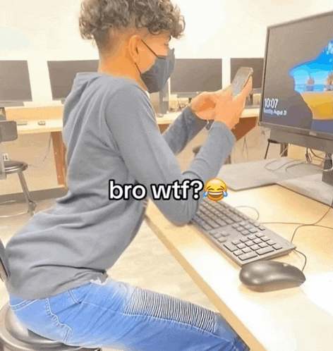 a person wearing a mask is sitting at a desk looking at their phone with the words bro wtf on the bottom