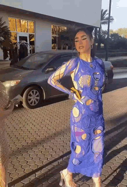 a woman in a blue dress is standing on a sidewalk in front of a car