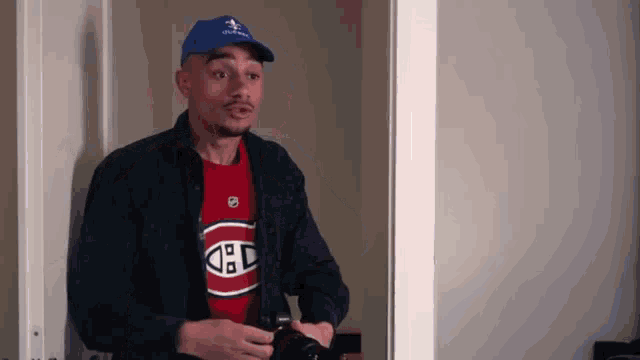 a man wearing a montreal canadiens shirt and a blue hat is holding a camera