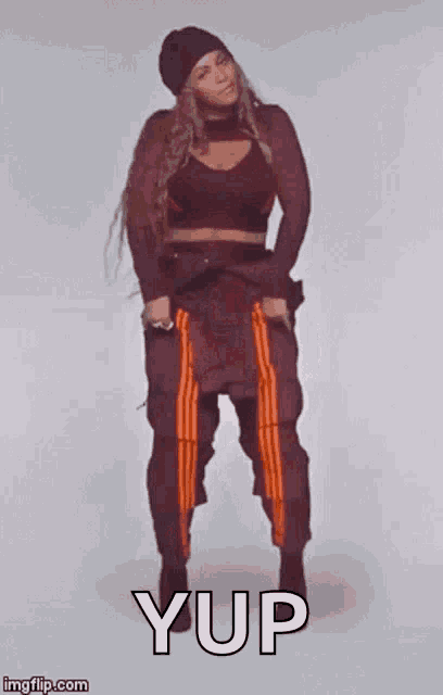 a woman in a crop top and orange pants is dancing with the words yup written on the bottom .