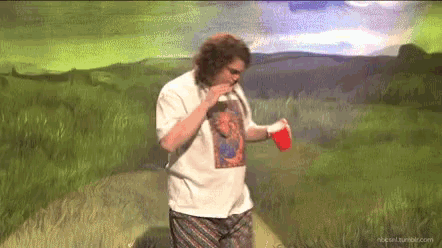 a man in a white shirt is standing in a field with a red cup in his hand .