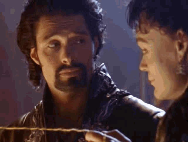 a man with a beard is looking at another man 's face while holding a rope .
